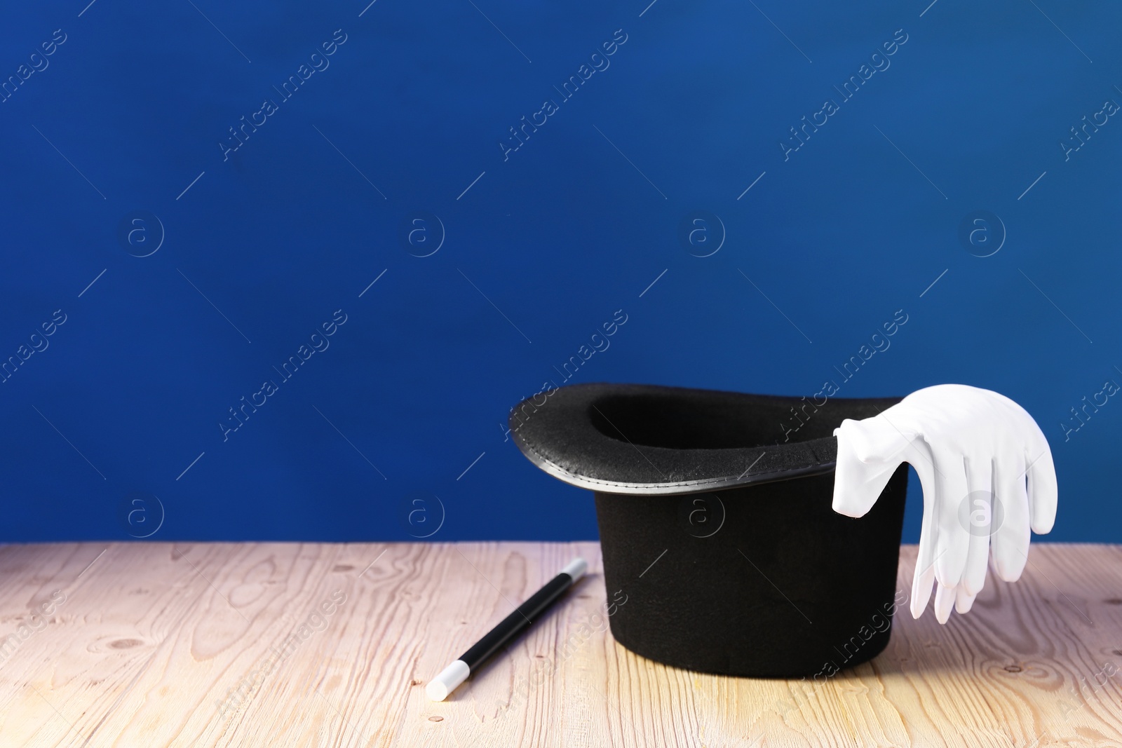 Photo of Magician's hat, wand and gloves on wooden table against blue background, space for text