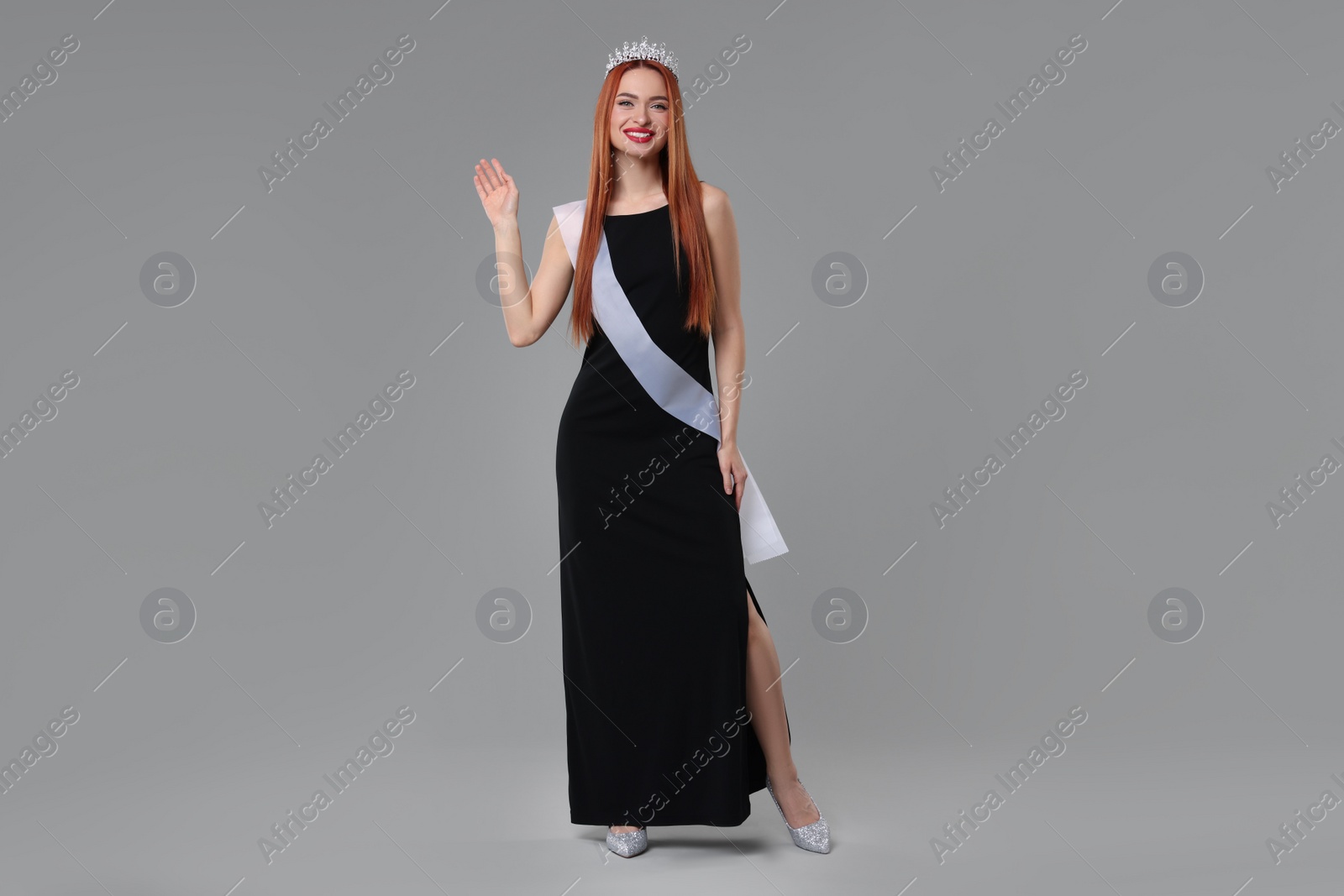 Photo of Beautiful young woman with tiara and ribbon in dress on light grey background. Beauty contest