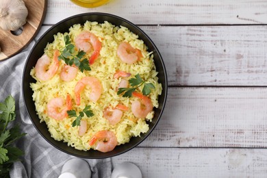 Photo of Delicious risotto with shrimps and parsley in bowl on white wooden table, flat lay. Space for text