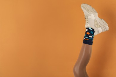 Woman wearing sneakers on orange background, closeup. Space for text