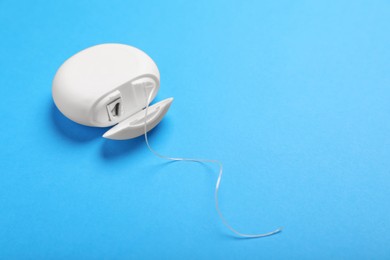 Photo of Container with dental floss on light blue background, closeup. Space for text