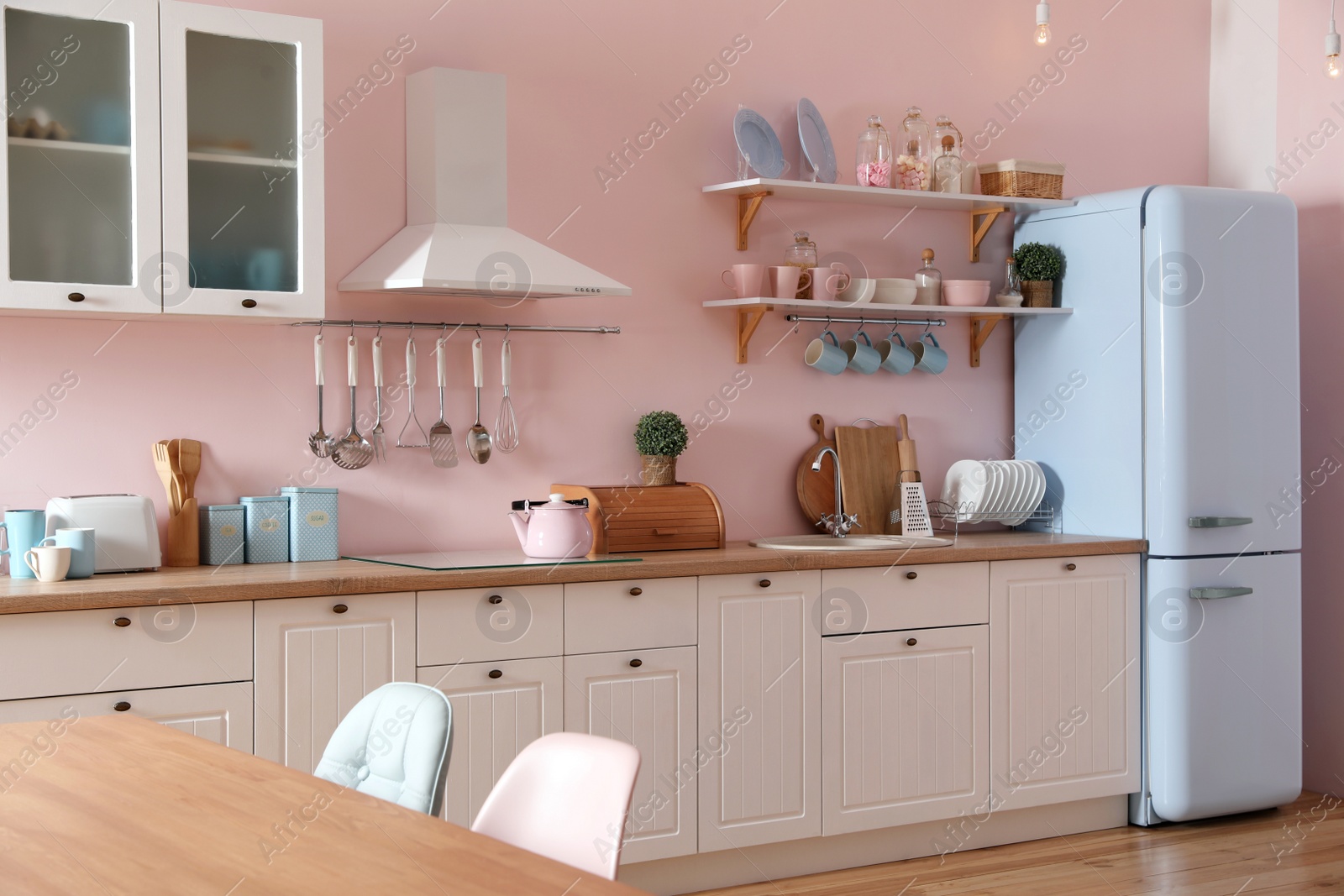 Photo of Stylish pink kitchen interior with dining table and chairs