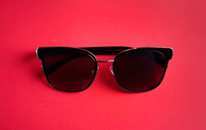 Stylish sunglasses on pink background, top view