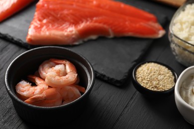 Shrimps in bowl and other ingredients for sushi on black wooden table, closeup