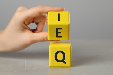 Woman turning cube with letters E and I above Q at light grey stone table, closeup