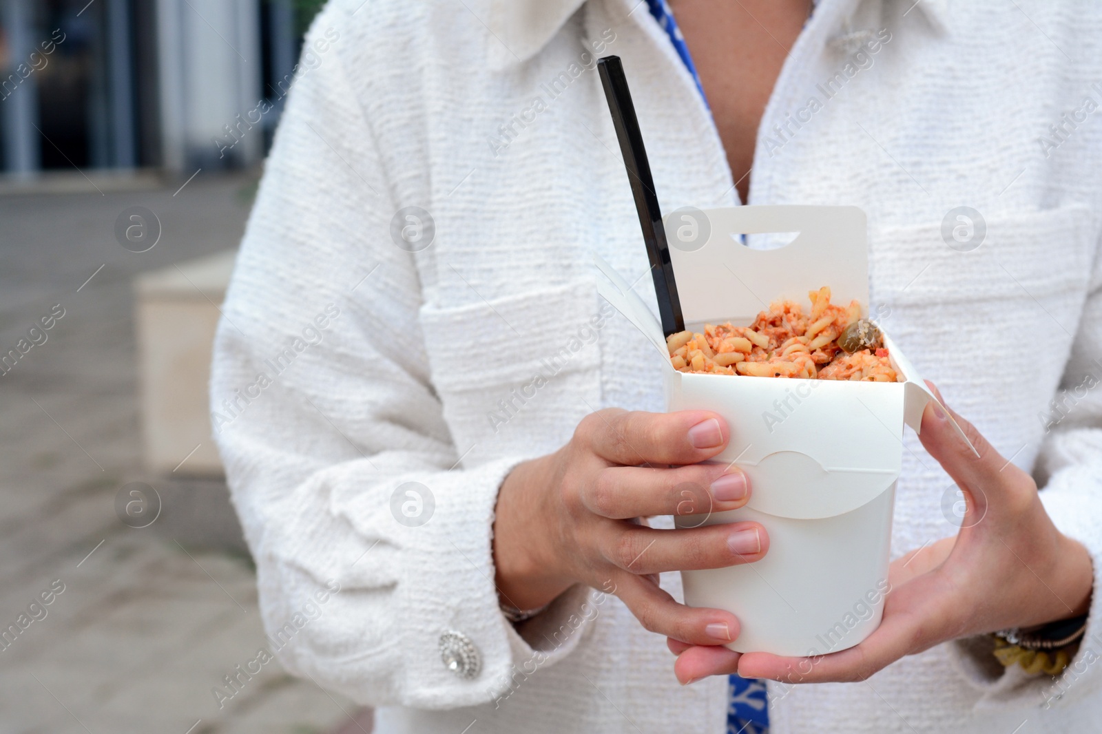 Photo of Woman holding paper box of takeaway noodles with fork outdoors, closeup. Street food