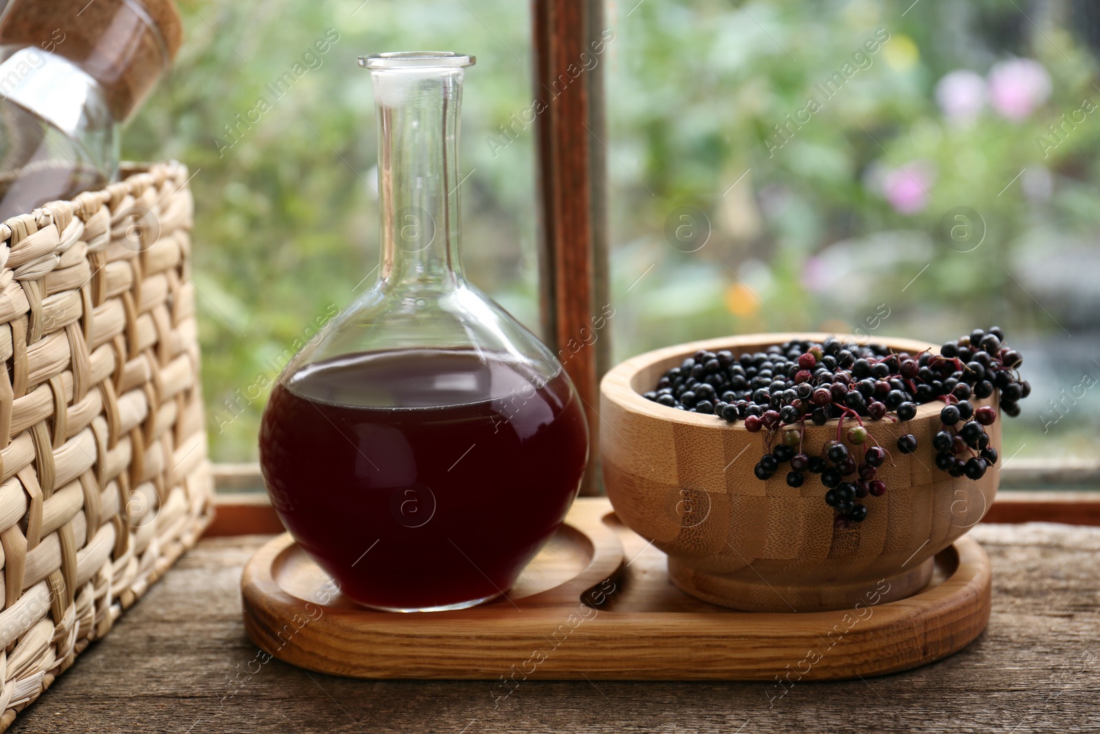 Photo of Elderberry wine and bowl with Sambucus berries on wooden table near window