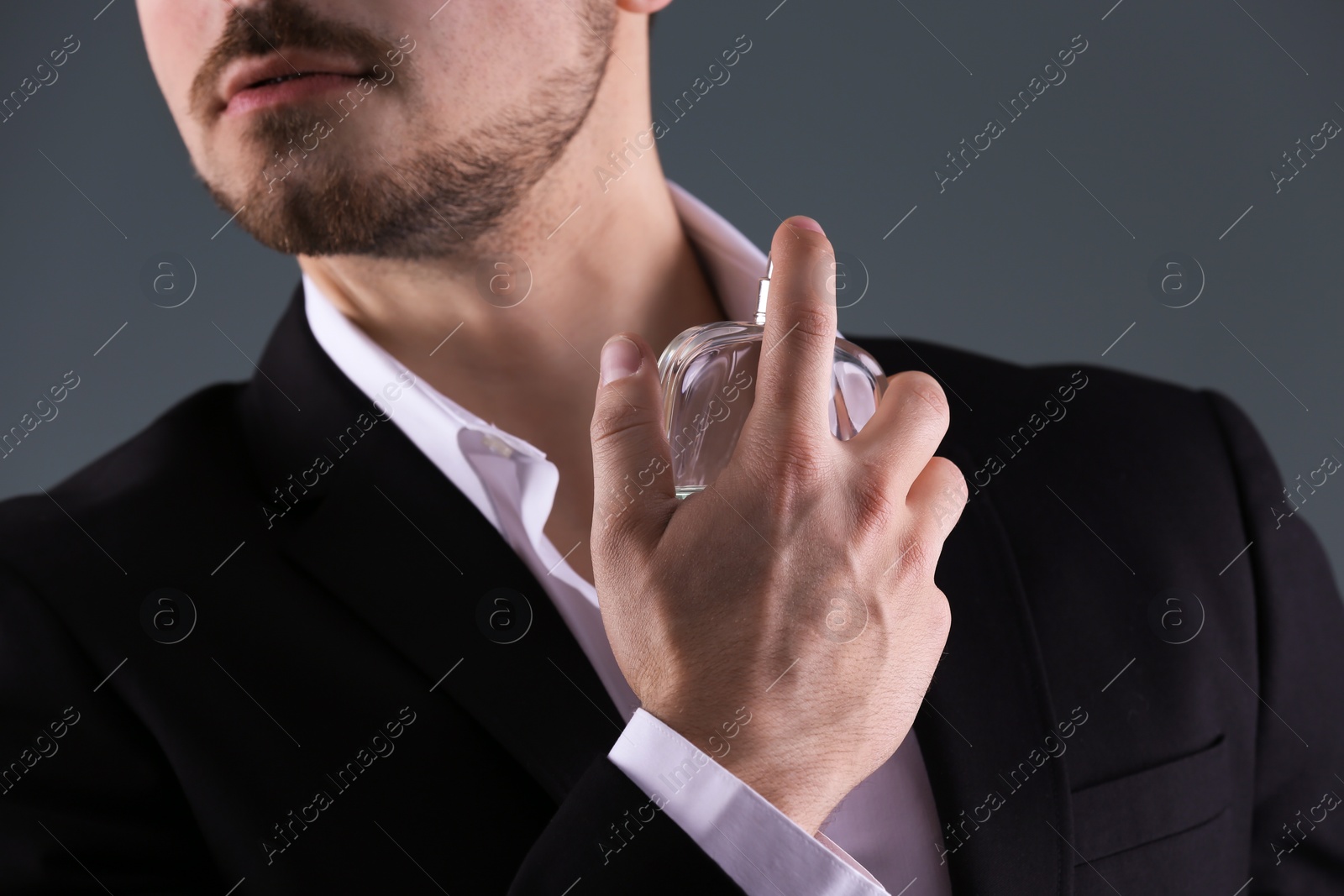 Photo of Handsome man in suit using perfume on dark background, closeup