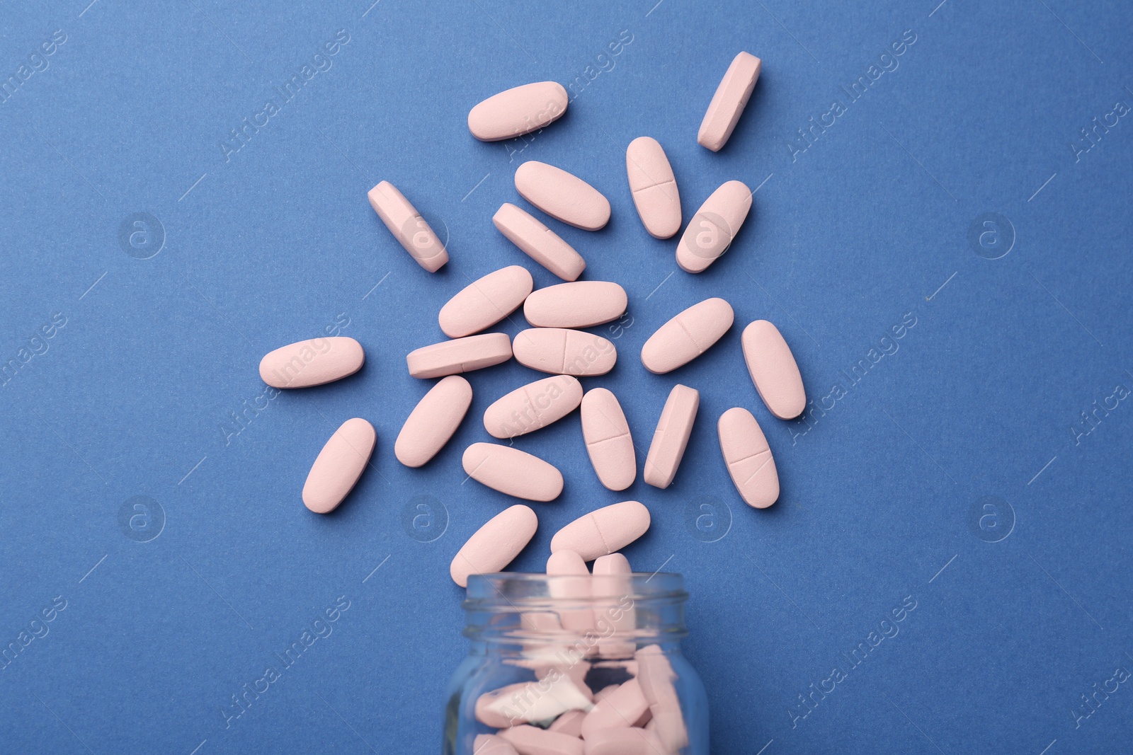 Photo of Bottle of pink vitamin capsules on blue background, top view