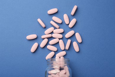 Bottle of pink vitamin capsules on blue background, top view