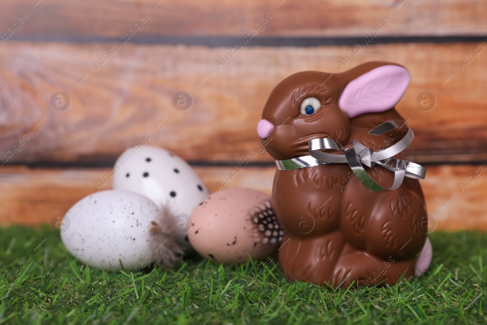 Photo of Easter celebration. Cute chocolate bunny and painted eggs on grass against wooden background. Space for text