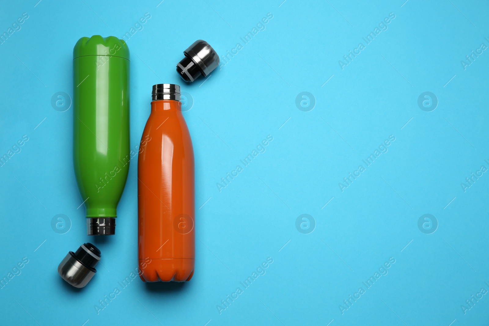 Photo of Modern thermo bottles on light blue background, flat lay. Space for text