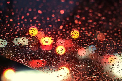 Photo of Blurred view of road through wet car window at night. Bokeh effect