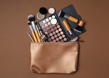 Cosmetic bag with makeup products and beauty accessories on brown background, flat lay