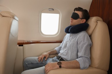 Photo of Young man with travel pillow and mask sleeping in airplane during flight