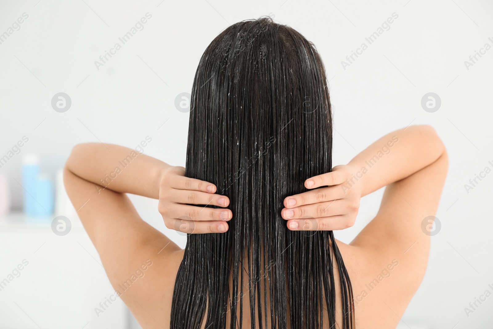 Photo of Woman applying hair conditioner in light bathroom