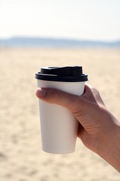 Photo of Woman with takeaway coffee cup on beach, closeup