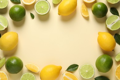 Frame of fresh ripe lemons, limes and green leaves on beige background, flat lay. Space for text