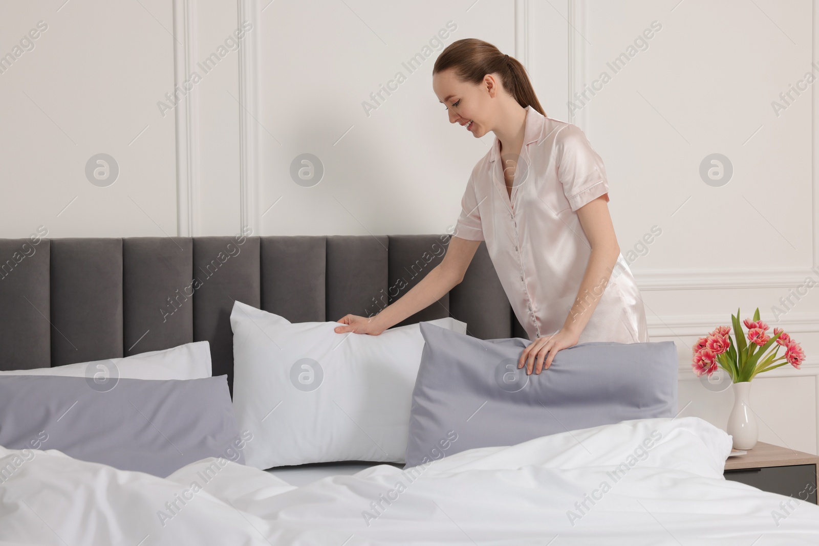 Photo of Young beautiful woman making bed in room