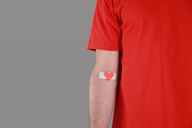 Photo of Blood donation concept. Man with adhesive plaster on arm against grey background, closeup. Space for text