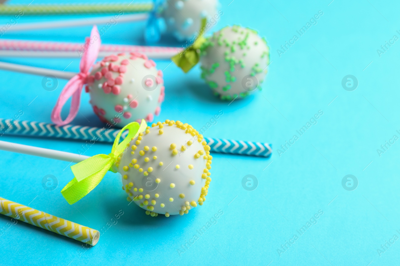 Photo of Tasty cake pops and straws on light blue background. Space for text