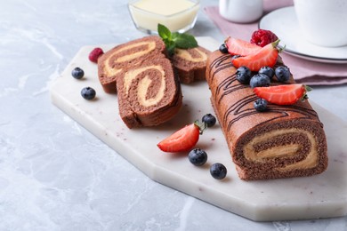 Photo of Tasty chocolate cake roll with cream and berries on light grey marble table