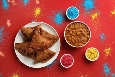 Photo of Traditional Indian food and color powder dyes on red background, flat lay. Holi festival