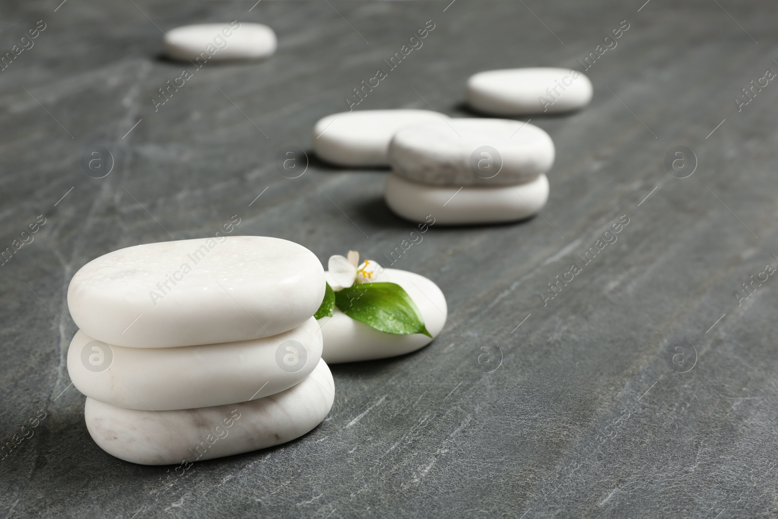 Photo of Stacked spa stones with flower and leaves on grey table. Space for text