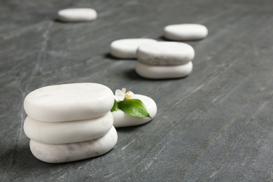 Stacked spa stones with flower and leaves on grey table. Space for text