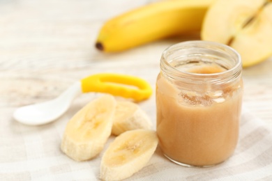 Jar with healthy baby food and cut banana on table