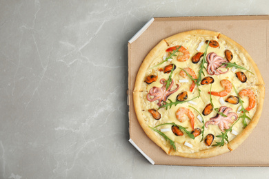 Delicious seafood pizza  in cardboard box on grey marble table, top view. Space for text