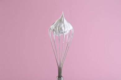 Whisk with whipped cream on pink background