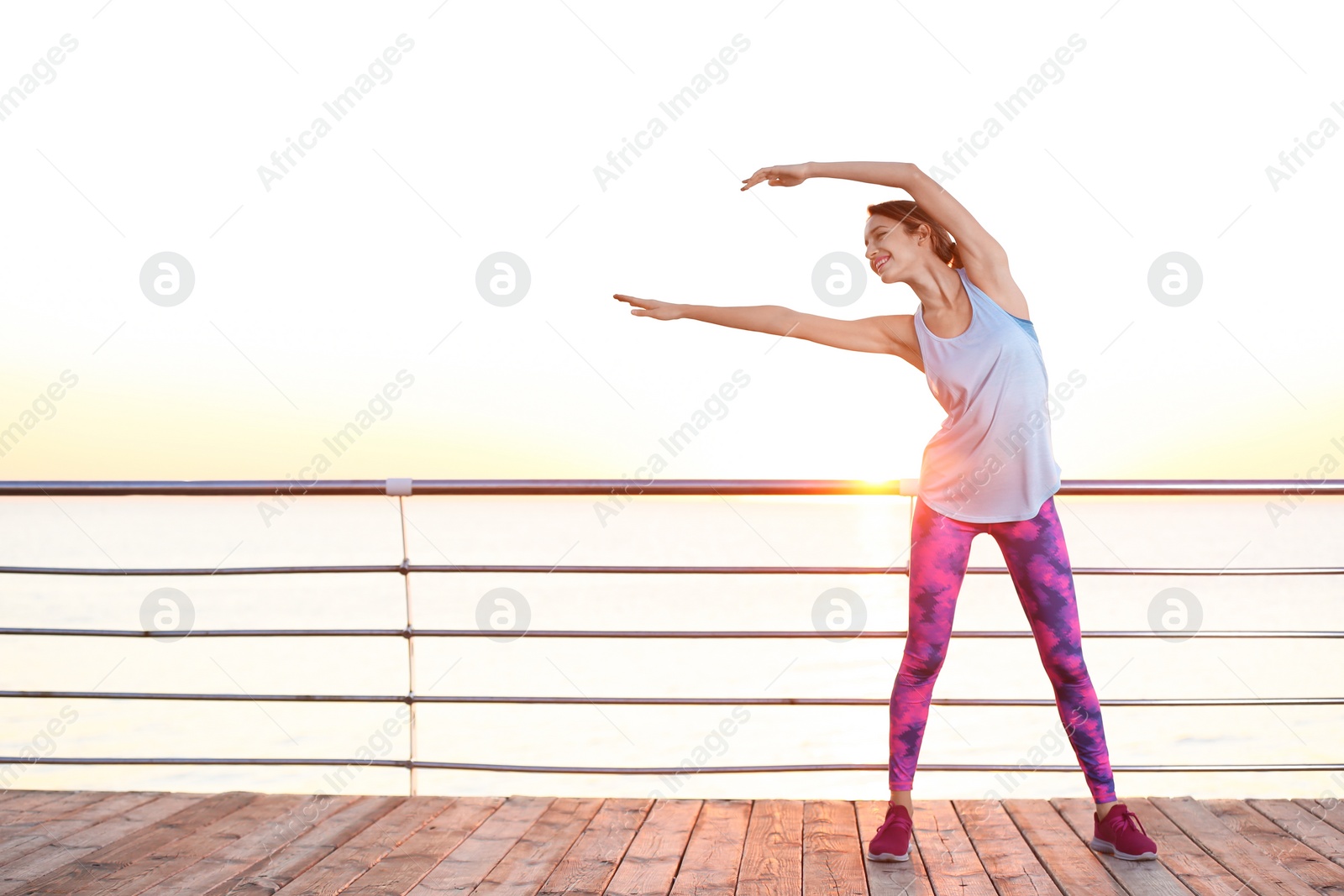 Photo of Young woman doing fitness exercises on pier in morning