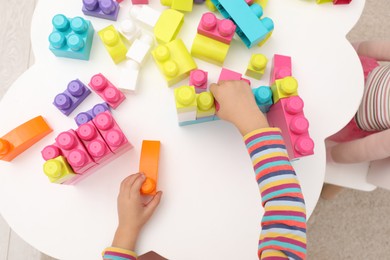 Cute little girl playing with colorful building blocks at table indoors, top view