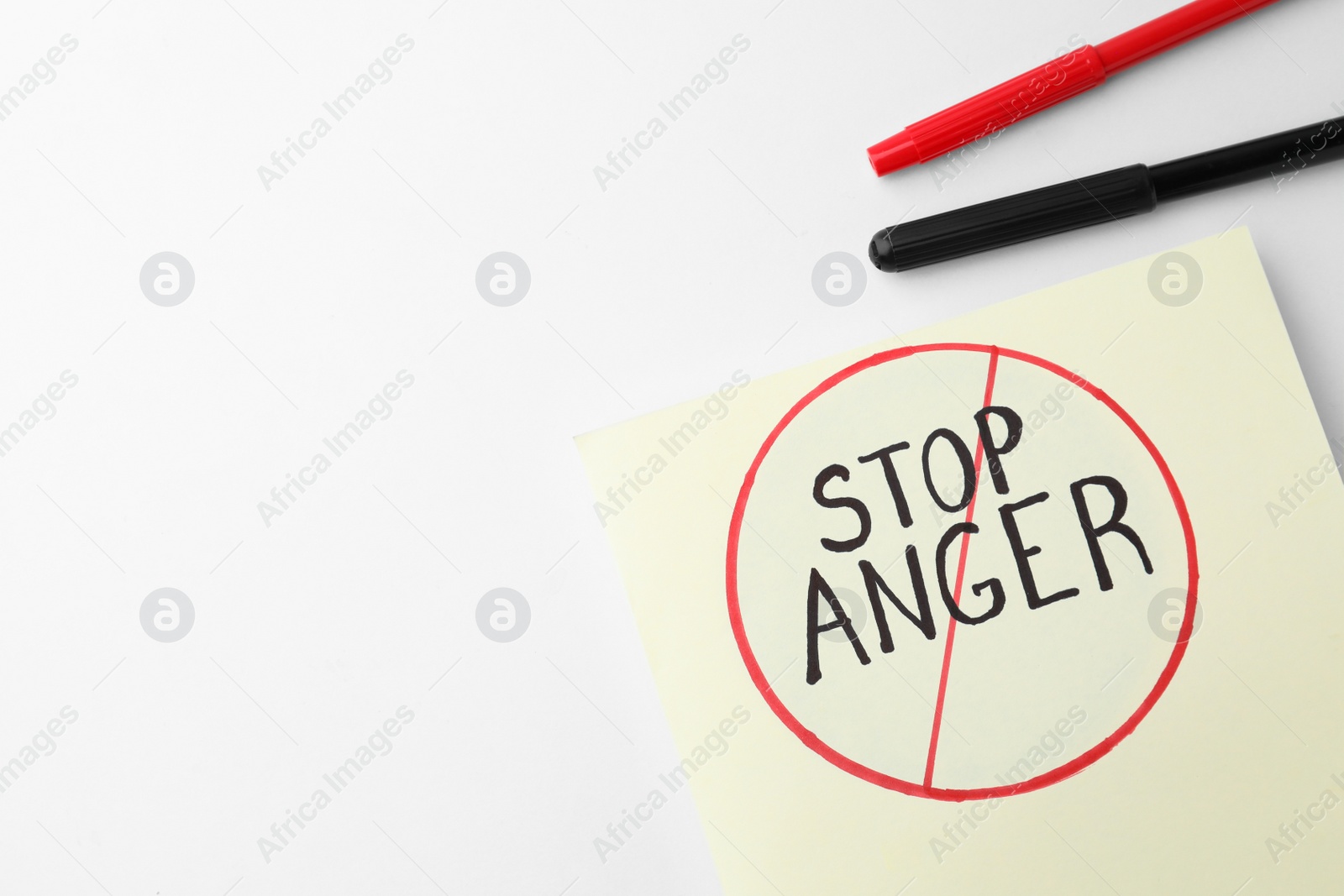 Photo of Black and red felt tip pens near sheet of paper with crossed over inscription Stop Anger on white background, flat lay. Space for text