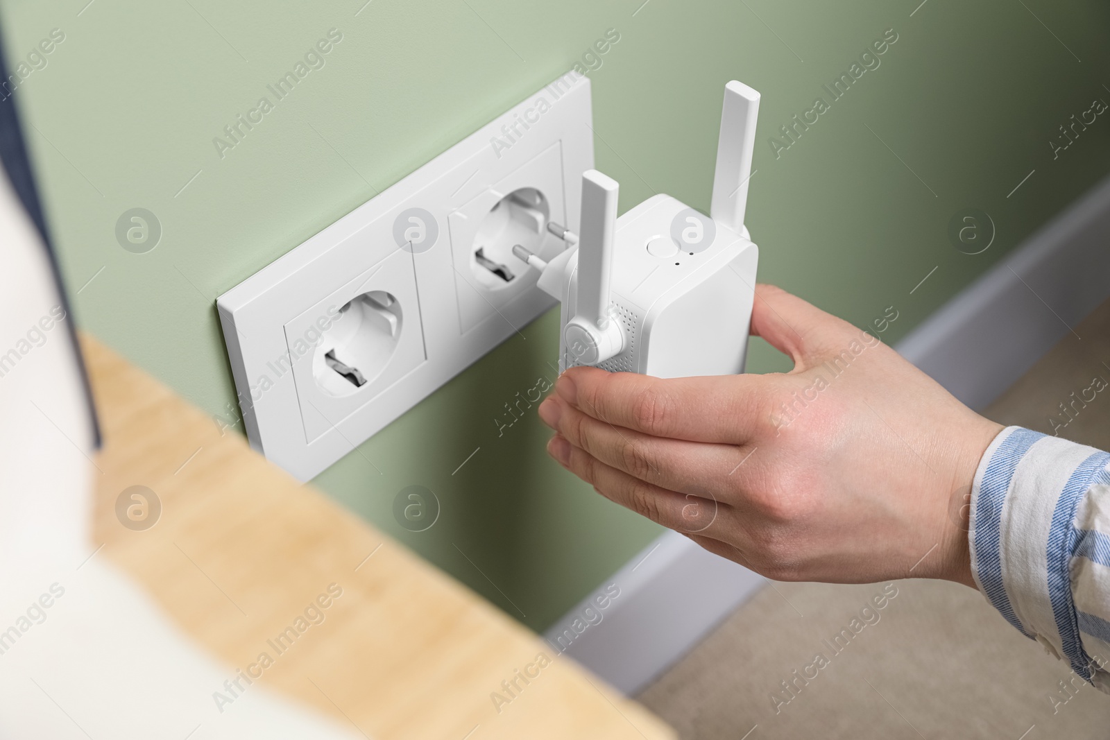 Photo of Woman inserting wireless Wi-Fi repeater into power socket indoors, closeup