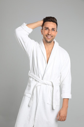 Happy young man in bathrobe on light grey background