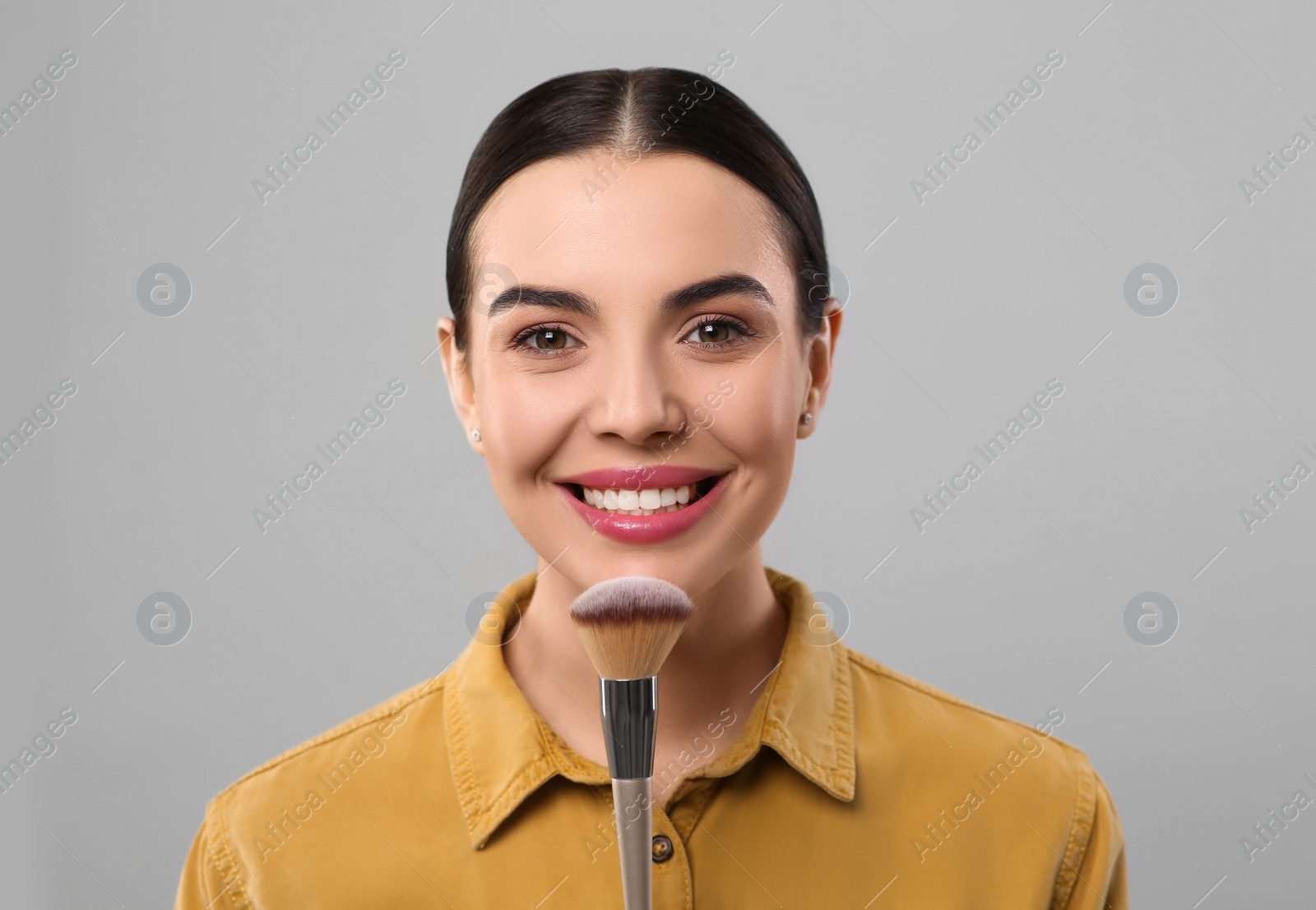 Photo of Happy woman with makeup brush on light grey background