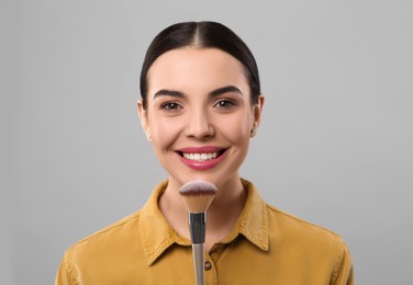 Happy woman with makeup brush on light grey background