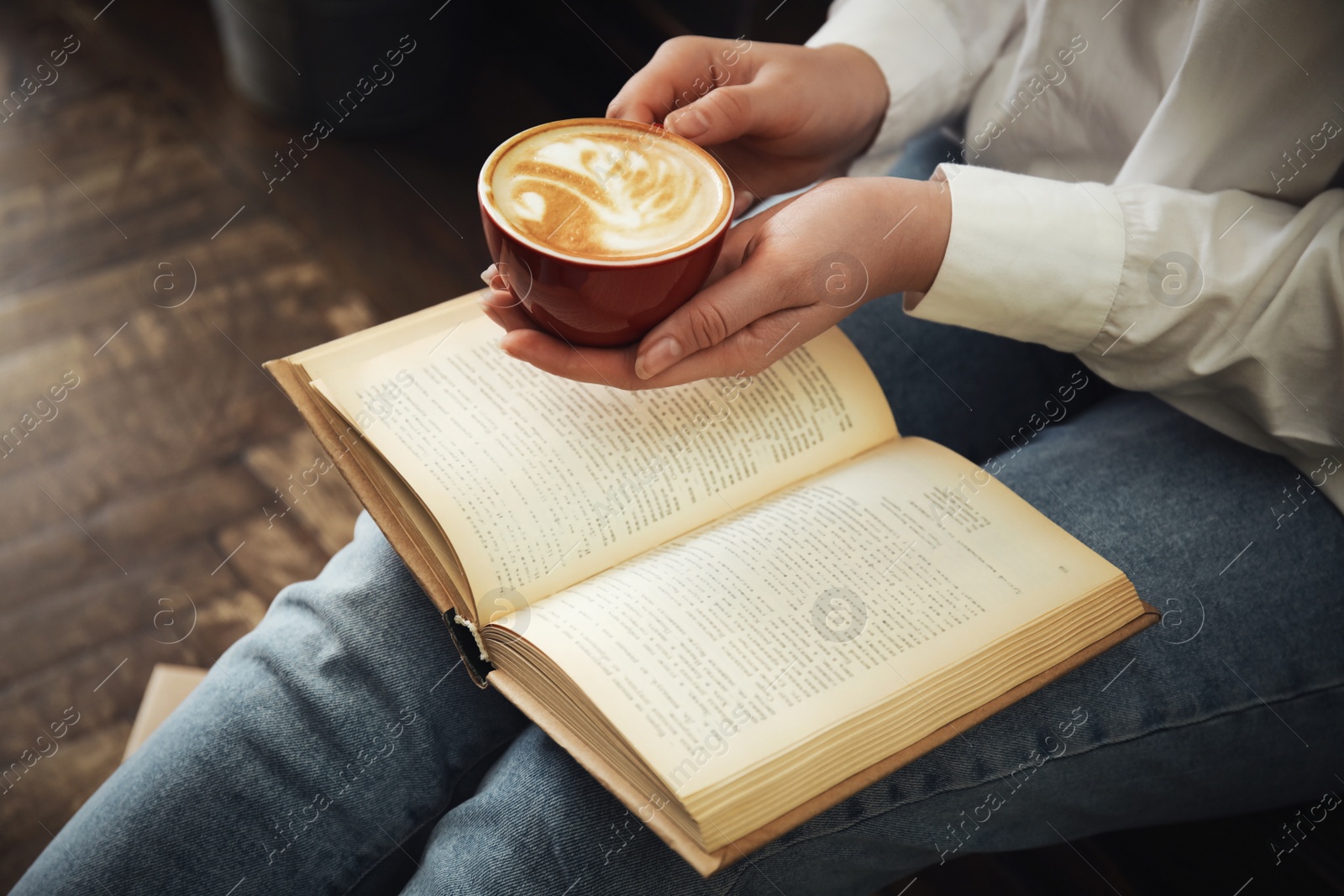 Photo of Woman with cup of coffee reading book indoors, closeup