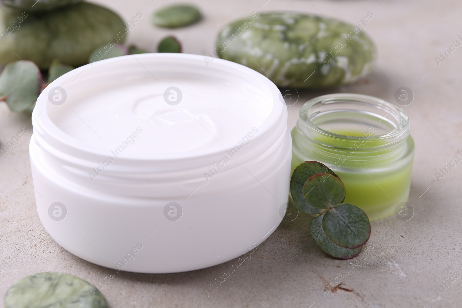 Photo of Jars of cream and green leaves on light textured table. Body care products