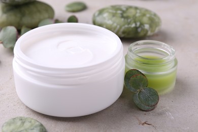 Photo of Jars of cream and green leaves on light textured table. Body care products