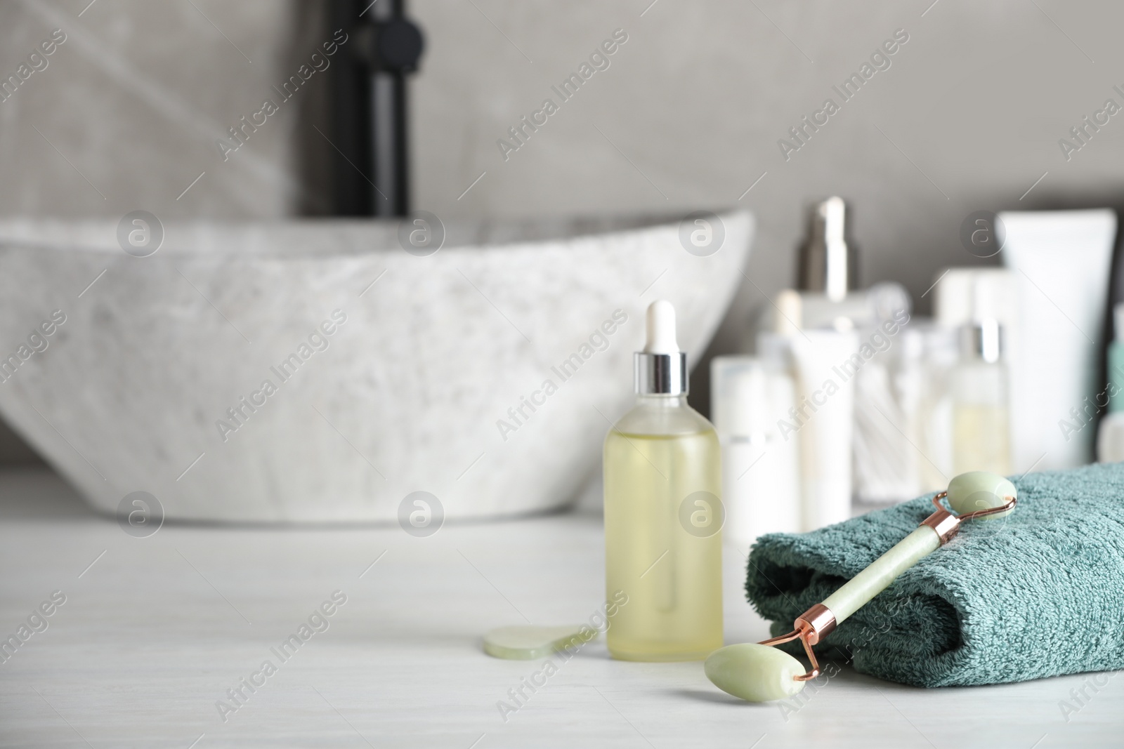 Photo of Natural face roller, gua sha tool and cosmetic products on counter in bathroom. Space for text