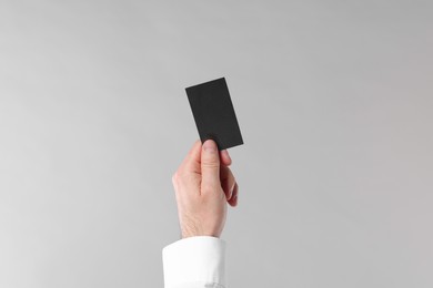 Man holding blank business card on light grey background, closeup