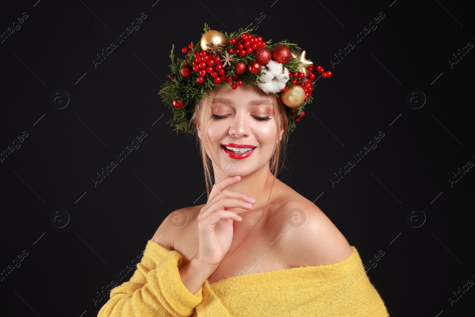 Photo of Beautiful young woman wearing Christmas wreath on black background