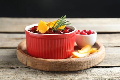 Photo of Fresh cranberry sauce in bowl, berries, rosemary and orange peels on wooden table