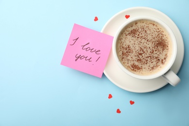 Photo of Paper with words I Love You, coffee and small red hearts on light blue background, flat lay. Space for text