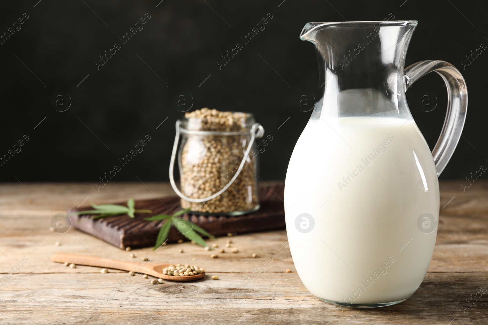 Photo of Composition with pitcher of hemp milk on wooden table against black background. Space for text
