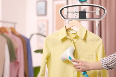 Woman steaming shirt on hanger at home, closeup. Space for text