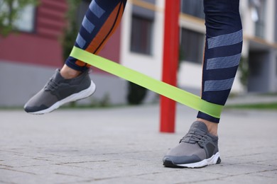 Photo of Woman doing exercise with fitness elastic band outdoors, closeup